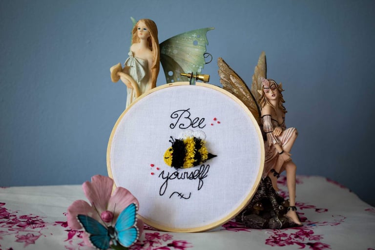 Product image of "Bee Yourself" embroidered bumble bee set against blue backdrop surrounded by fairies and a butterfly