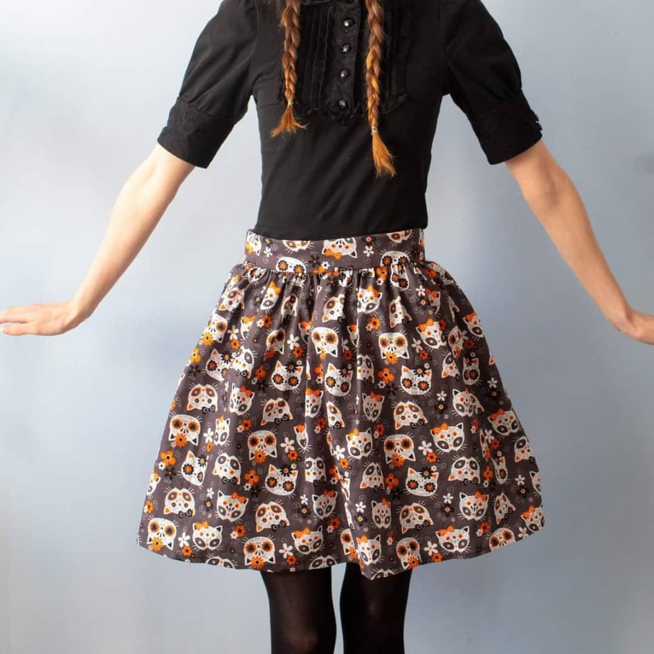 Product image of model wearing Tabby skirt with a print of white cat skulls and orange accents on a black background