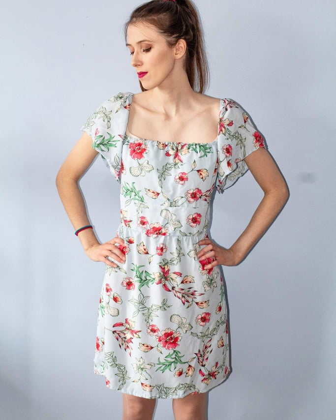 Product image of smiling model wearing Callisto dress in a print of pink flowers on a pale blue background