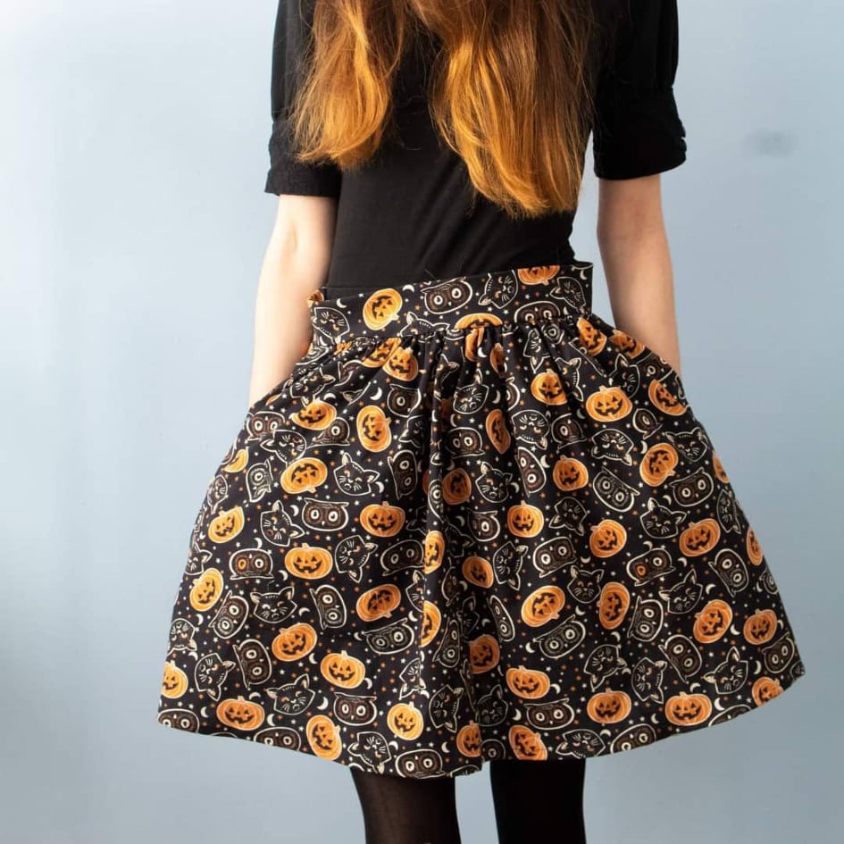 Product image of model wearing Tabby skirt with a print of black cats, black owls and orange pumpkins on a black background