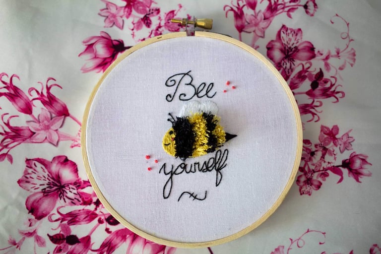Product image of "Bee Yourself" embroidered bumble bee set against white and pink floral backdrop