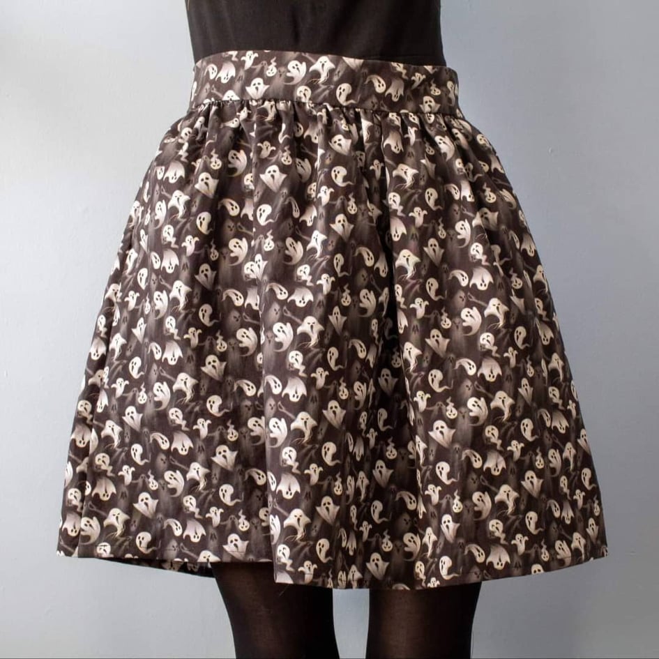 Product image of model wearing Tabby skirt with a print of white ghosts on a black bakcgroung